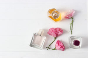 Três frascos de perfume em formatos e tons diferentes com rosas cor-de-rosa sobre fundo branco de madeira