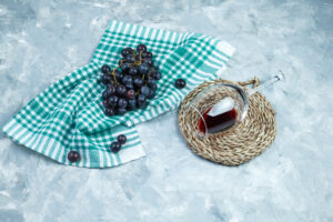 Cacho de uvas tintas ao lado de uma taça de vinho tinto sobre pano xadrez verde