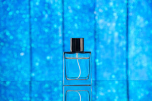 Frasco de perfume transparente com tampa preta sobre superfície refletora em fundo azul brilhante